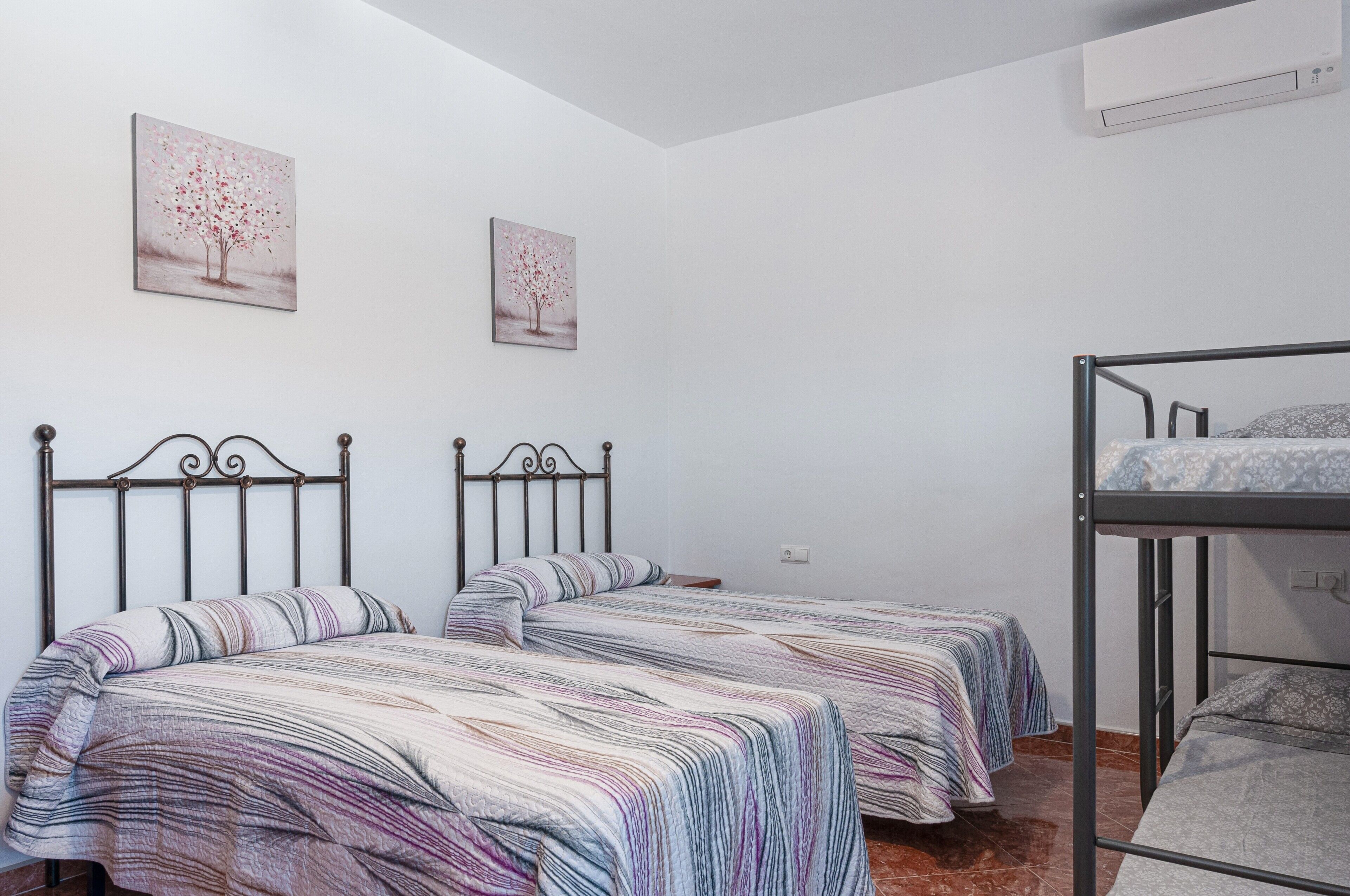 A room with two beds, a bunk bed, white walls, and two paintings.