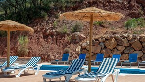 A poolside area with lounge chairs and umbrellas, surrounded by a rocky landscape. - Vacation Home "Sunset El Tejar" with Mountain View, Private Pool & Wi-Fi (Almogia)
