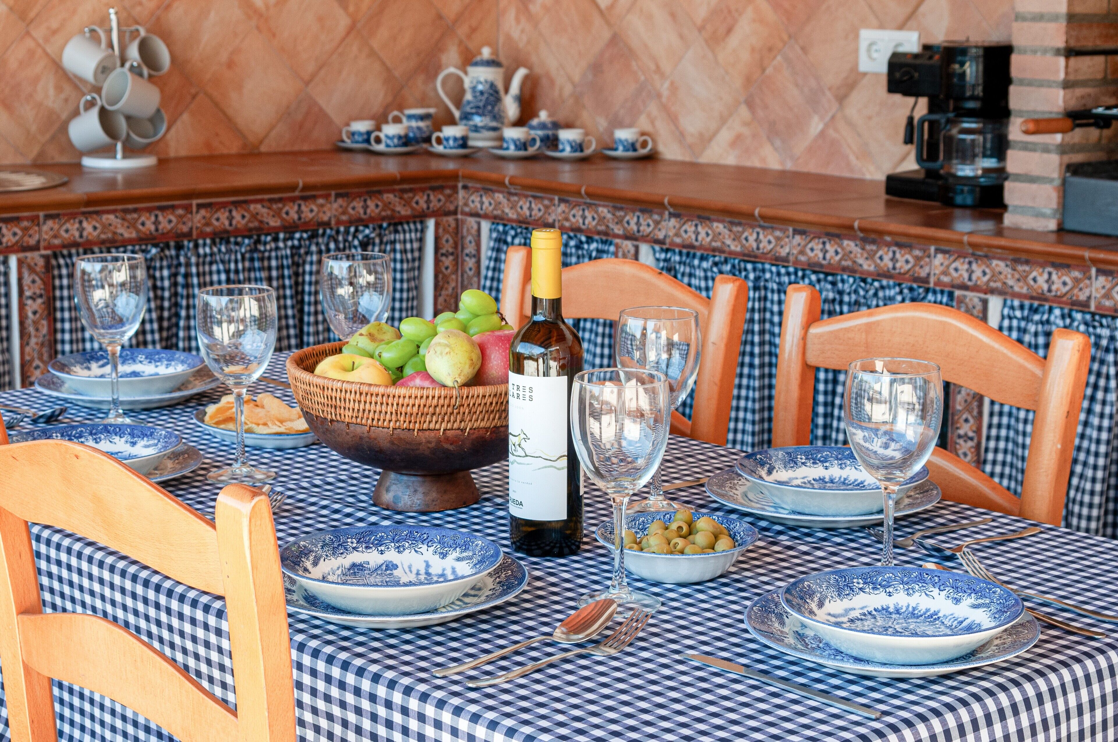 Een eettafel gedekt met blauwe en witte borden, een fles wijn en een schaal fruit.
