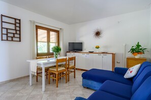 Un salon comprenant un téléviseur, un canapé, une table à manger, des chaises et un coin cuisine.