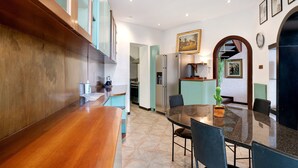 A modern kitchen with a wooden bar, a dining table with chairs, and a refrigerator. - Villa 'Capriccio' with Sea View, Private Terrace and Private Garden (Bordighera)