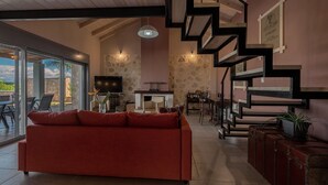 A spacious living area with a red sofa, a staircase, and a stone wall. - Villa Manolia (Πρέβεζα)