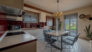 A modern kitchen with a central island, built-in appliances, and a dining area with a chandelier. - Villa Manolia (Πρέβεζα)