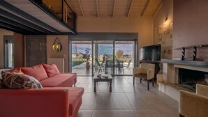 A spacious living room with a red sofa, a fireplace, and a television. - Villa Manolia (Πρέβεζα)
