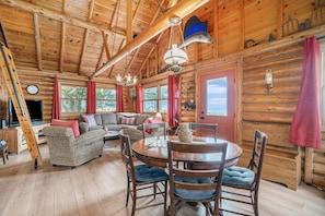 Cozy cabin interior with a rustic charm, featuring a round dining table, comfortable sofa, and large windows.
