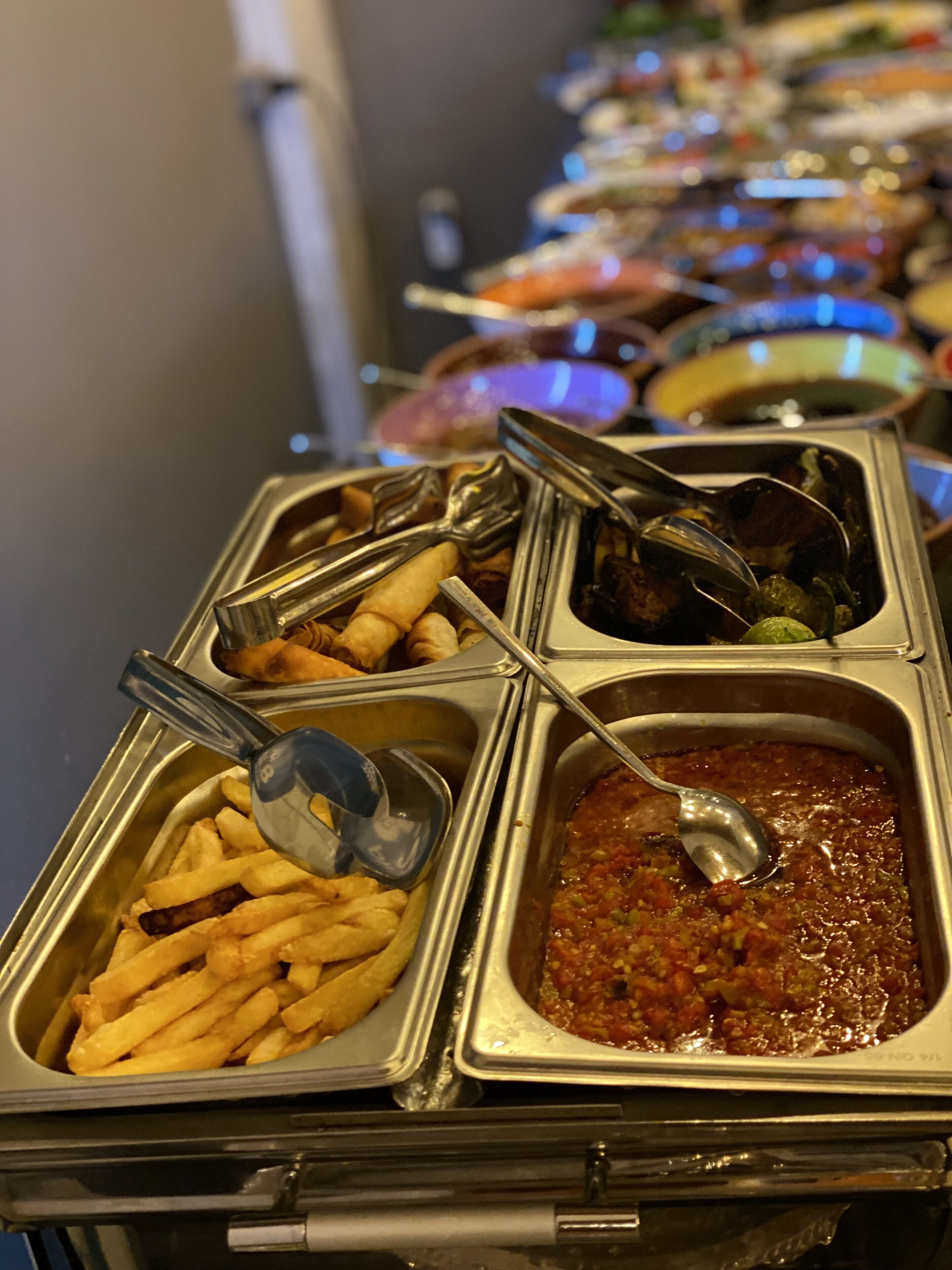 A buffet with various food items including French fries, a tomato-based dish, and other prepared foods in metal containers.