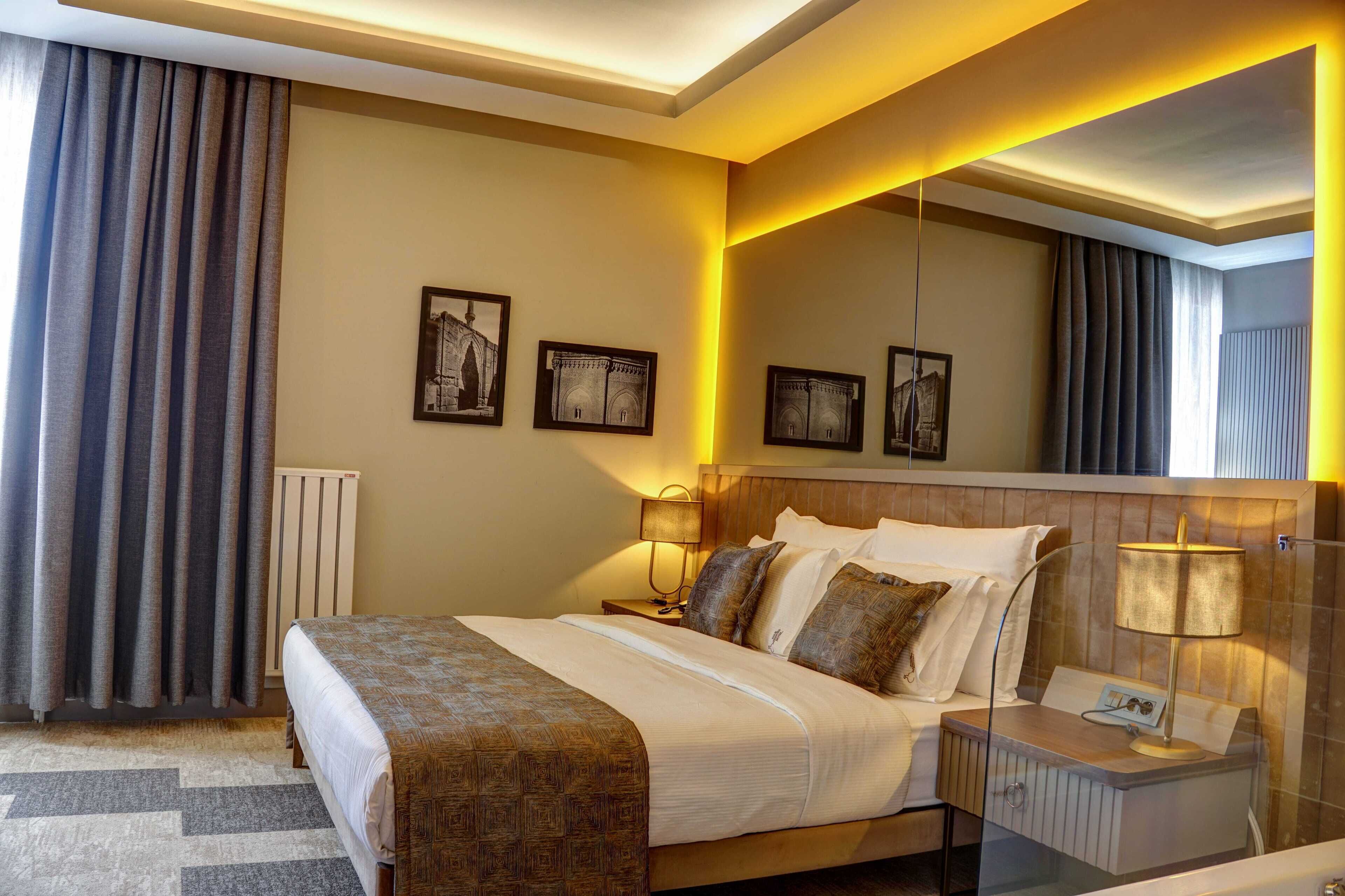 A hotel room with a large bed, two bedside tables, a nightstand, and a wall-mounted lamp. There are three framed pictures on the wall.
