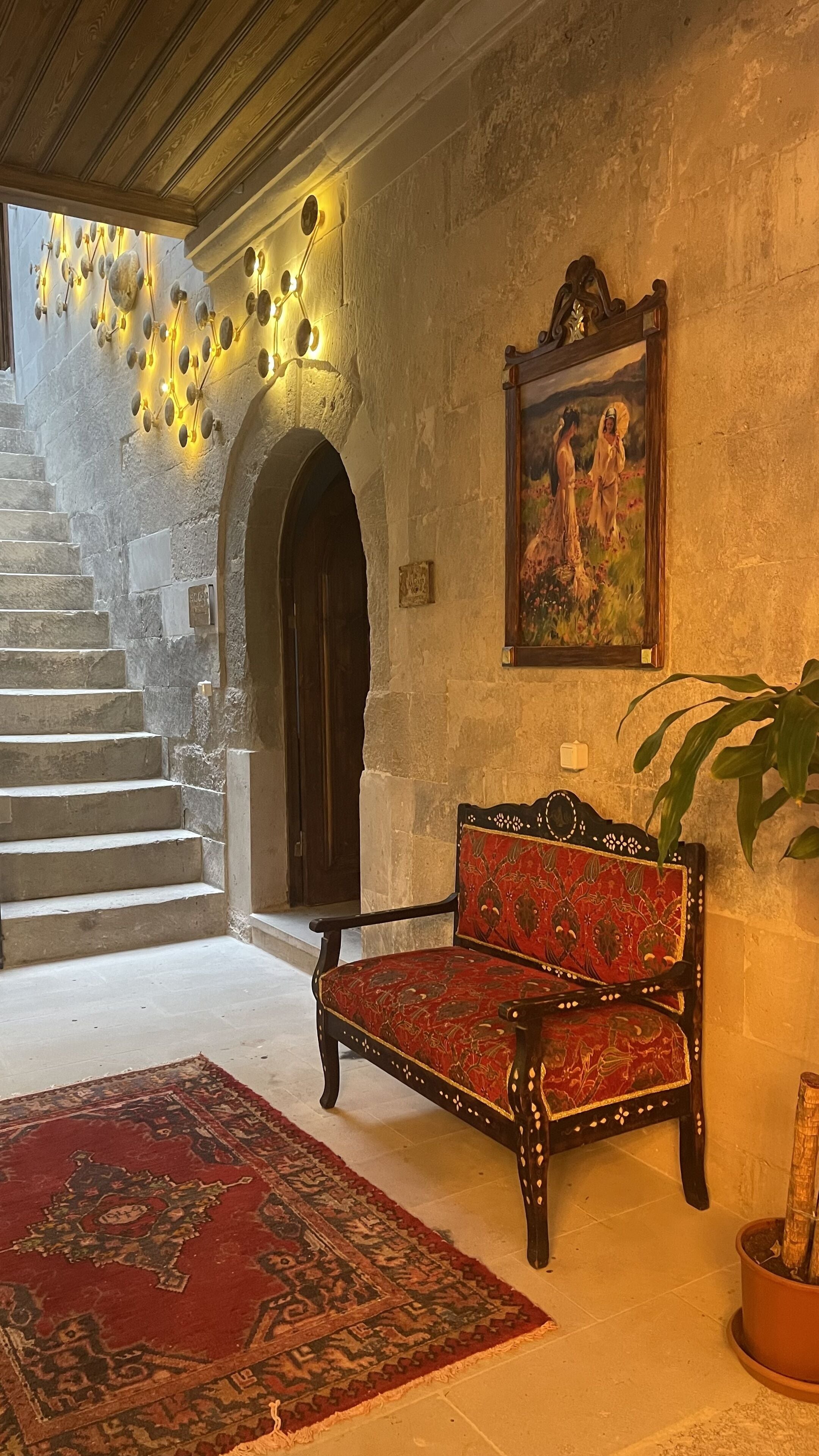 A stone staircase leading to a balcony, a red patterned sofa, a large painting, and a potted plant.