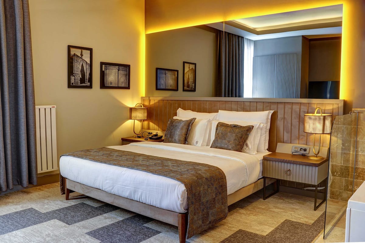 Une chambre d’hôtel avec un grand lit, deux tables de chevet, une commode, un miroir et des tableaux encadrés accrochés au mur.