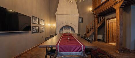Una larga mesa de comedor con un camino rojo, rodeada de sillas de cuero, en una habitación con vigas de madera y un candelabro.