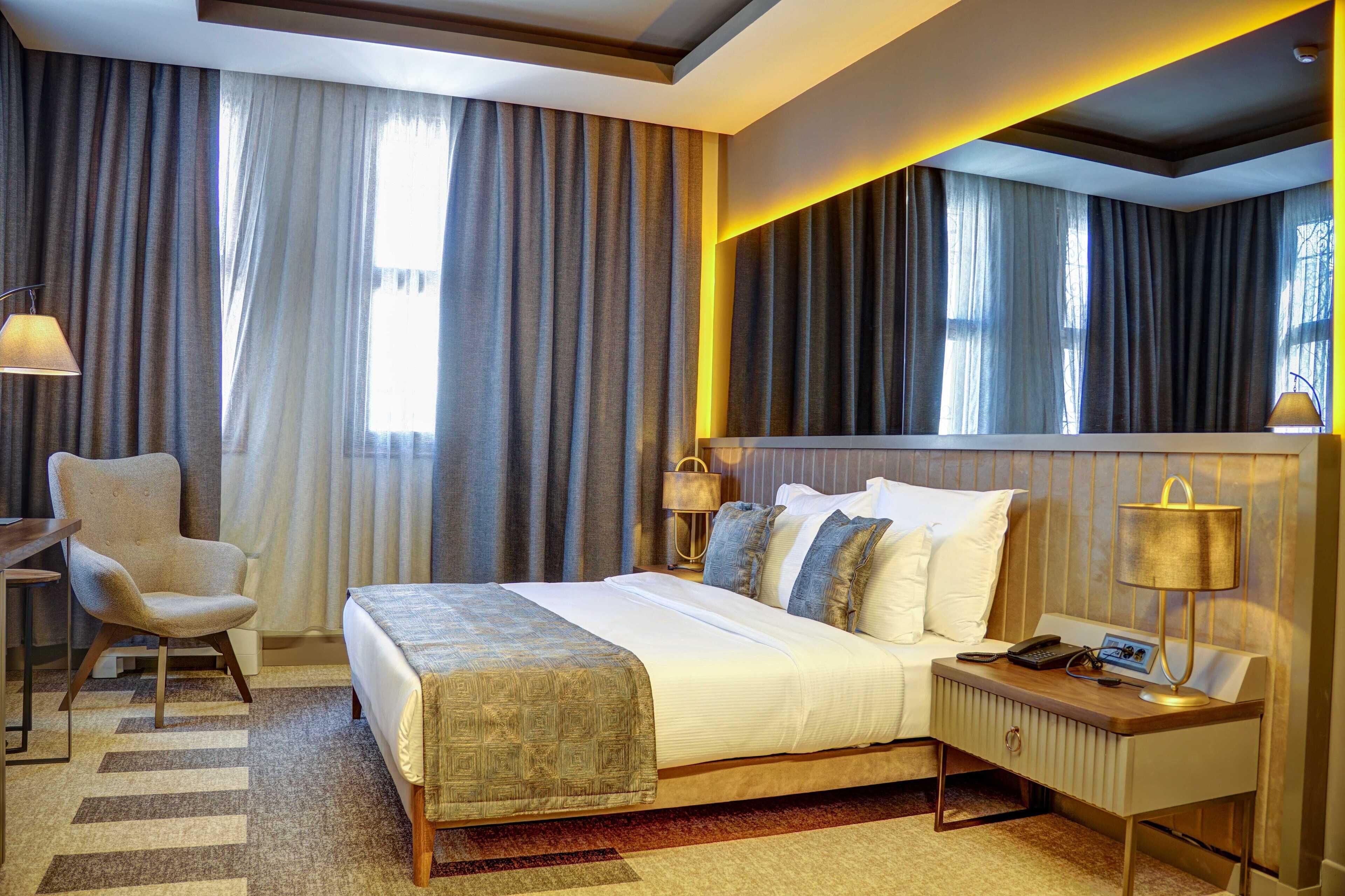 A hotel room with a large bed, a desk with a lamp, and a chair.