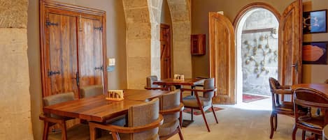 A dining area with wooden tables and chairs, stone walls, and arched doorways.