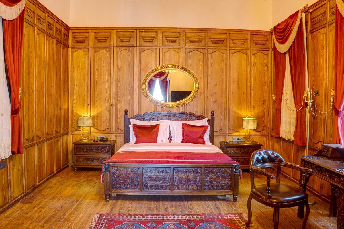 Une chambre à coucher traditionnelle en bois, avec un lit à baldaquin, un miroir rond au-dessus du lit et une table de chevet classique en bois, sur laquelle se trouve une lampe.