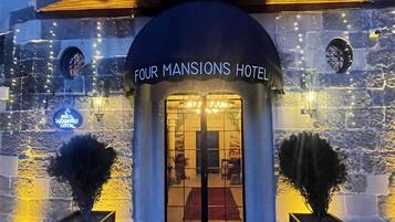 The exterior of Four Mansions Hotel with a stone facade, a red carpet entrance, and two potted plants.