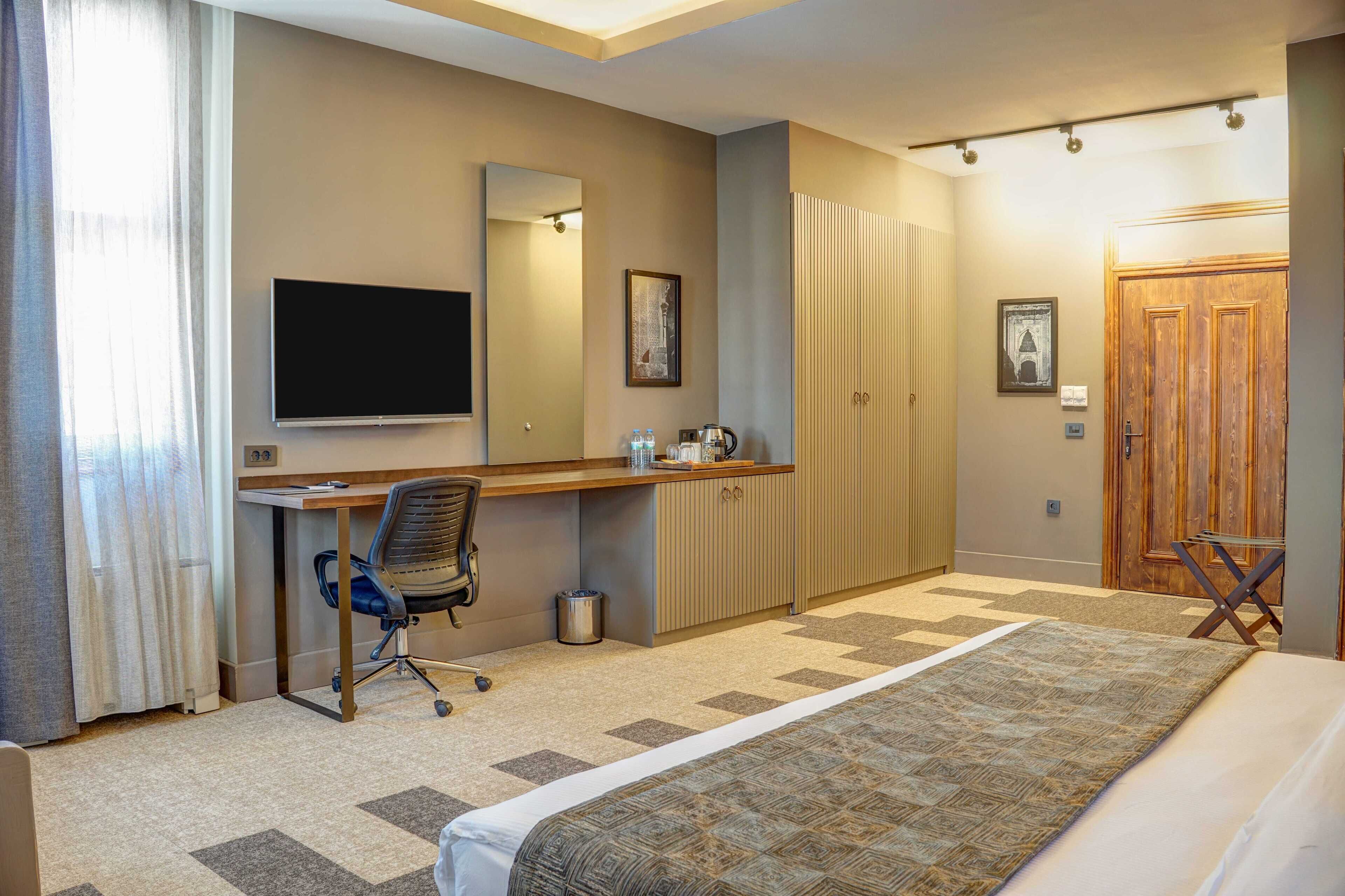 A hotel room with a bed, desk, chair, TV, wardrobe, and a door.