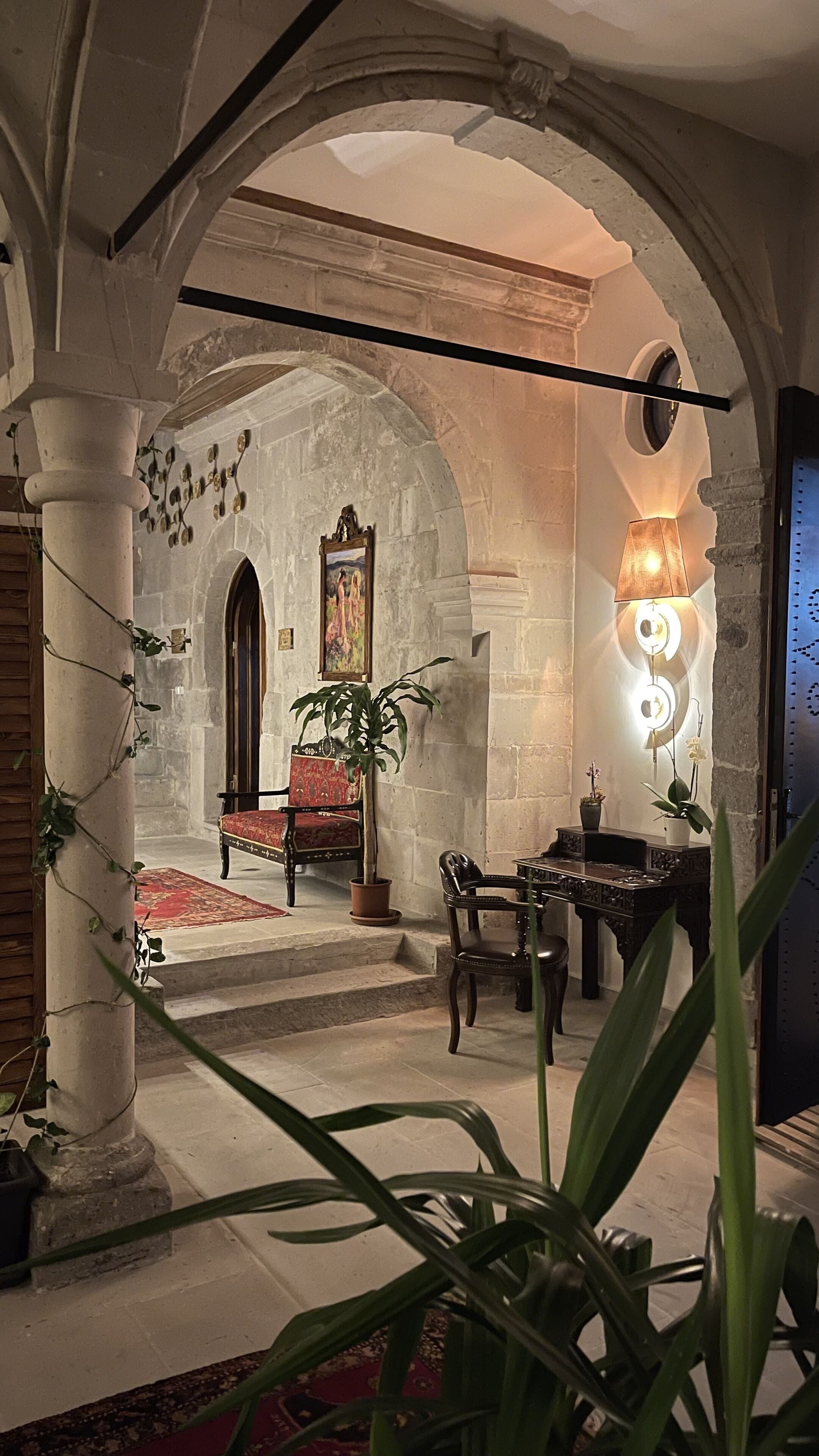 Un interior con un arco de piedra, una silla roja, una mesa y una lámpara.