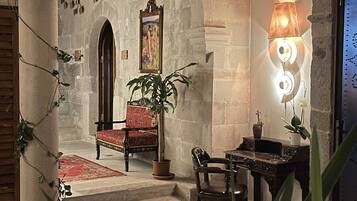 Un interior con un arco de piedra, una silla roja, una mesa y una lámpara.