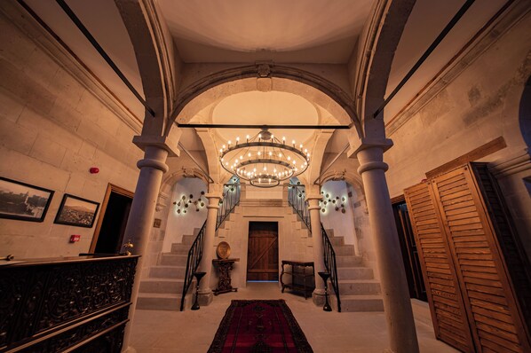 An interior with a grand staircase, a chandelier, and a red carpet.