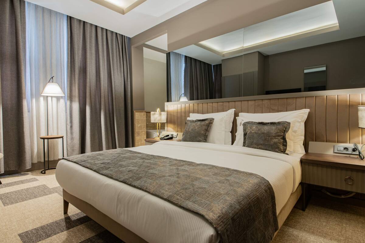 Une chambre d’hôtel avec un grand lit, une table de chevet avec une lampe, une petite table à côté du lit et un miroir au-dessus du lit.