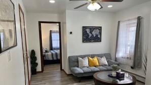 A living room with a grey sofa, a round coffee table, and a ceiling fan. - Quiet Apt with Coffee Bar, 1/2 Mile to West Point! (Highland Falls)