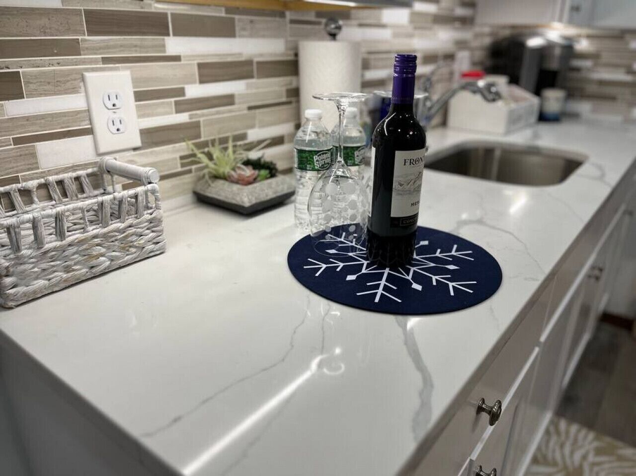 A kitchen counter with a wine bottle, glasses, and a decorative mat.