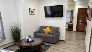 A living room with a grey sofa, a round coffee table, a TV mounted on the wall, and a large plant. - Quiet Apt with Coffee Bar, 1/2 Mile to West Point! (Highland Falls)