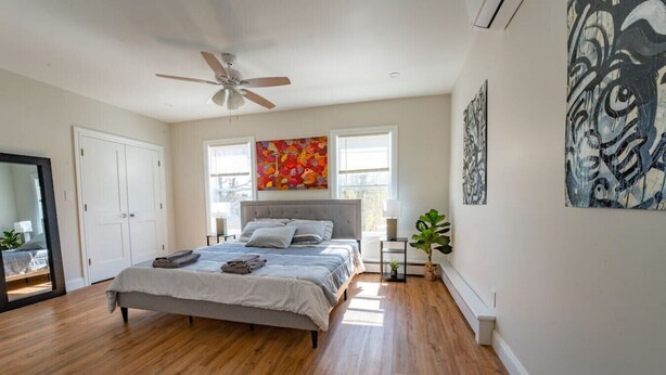 A bedroom with a bed, a ceiling fan, a window, and a painting on the wall. - Local Artist Inspired | Walk to WestPoint + King Bed (Highland Falls)