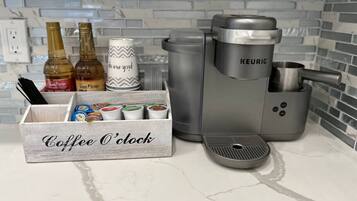 Una cafetera, un molinillo de café y un depósito para cápsulas de café sobre una encimera de cocina.