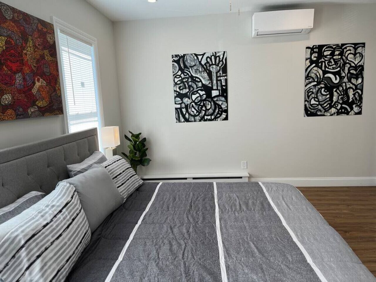 A bedroom with a bed, a window, and two abstract wall art pieces.