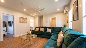 A living room with a green sectional sofa, a coffee table, and a ceiling fan. - Local Artist Inspired | Walk to WestPoint + King Bed (Highland Falls)