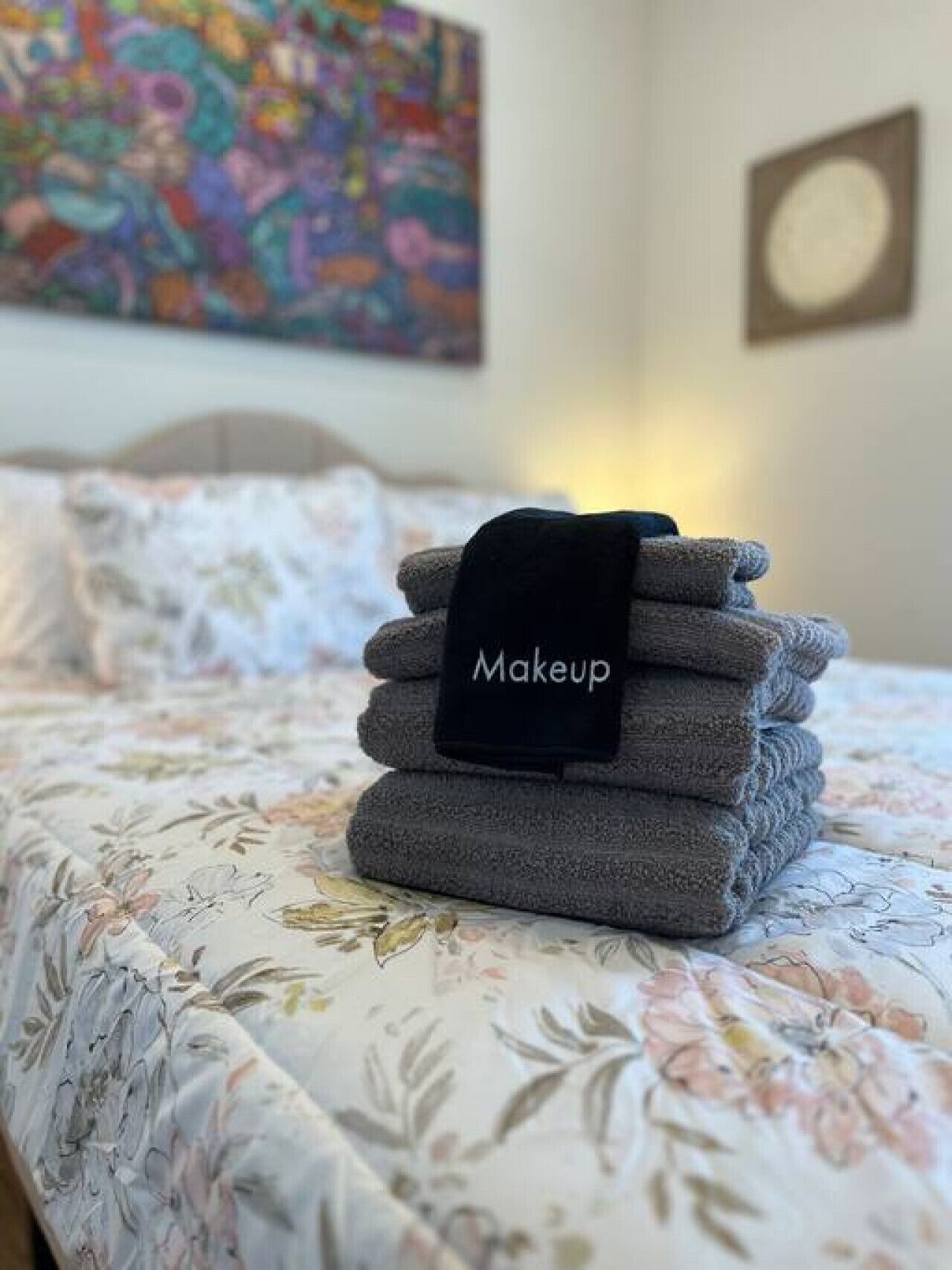 Een netjes opgevouwen stapel handdoeken met een etiket erboven, geplaatst op een bed met bloemenbedrukking.