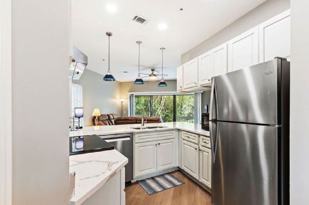 Cocina moderna con armarios blancos, refrigerador de acero inoxidable, luces colgantes y una ventana que ofrece luz natural.