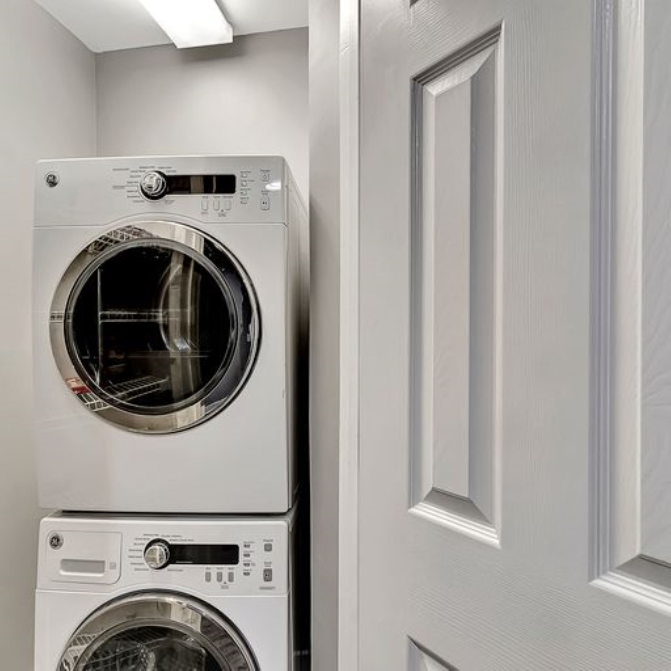 Una lavadora y secadora apiladas en una habitación con una puerta y paredes blancas lisas.
