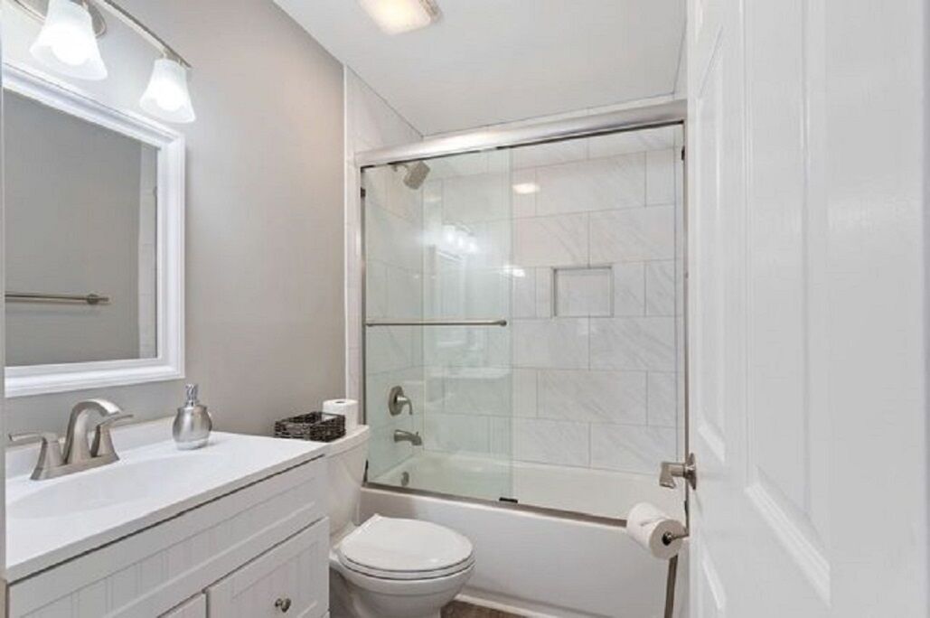 Un baño moderno con ducha de vidrio, lavamanos blanco y retrete.