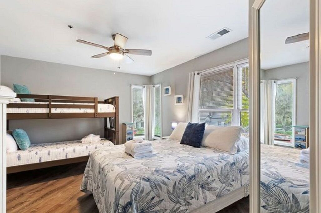 A bedroom with a bunk bed, a single bed, a ceiling fan, and large windows.