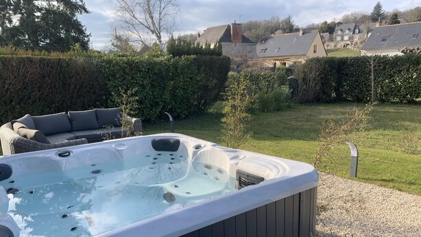 Un jacuzzi en un patio trasero con una terraza de madera, una zona de estar y vistas a casas al fondo.