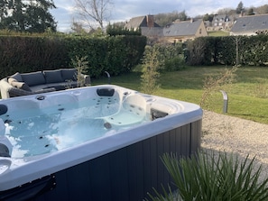 Un jacuzzi en un patio trasero con una terraza de madera, una zona de estar y vistas a casas al fondo.