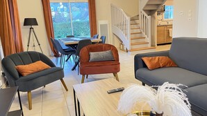 Una sala de estar moderna con un sofá, sillones, una mesa de centro y un comedor con una mesa y sillas. Una escalera conduce a un nivel superior.