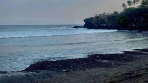 Una playa con costa rocosa, palmeras y cielo despejado con formaciones de nubes.