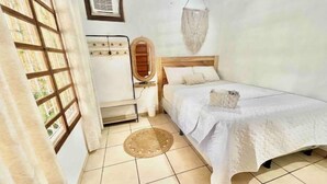 Una habitación pequeña y limpia con cama, espejo, ventana y aire acondicionado de pared.