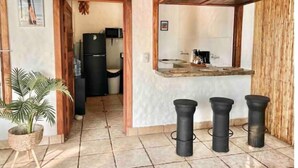 Cocina compacta con refrigerador, microondas y pileta. Hay tres taburetes y una planta en maceta.