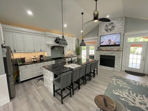 A modern kitchen with white cabinets, a central island, and a fireplace. - Downtown Westerly and Misquamicut Getaway with Beautiful Outdoor Kitchen (Westerly)