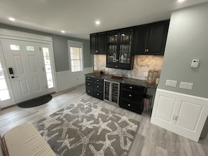 A modern kitchen with dark cabinets, a marble countertop, and a starfish-patterned rug. - Downtown Westerly and Misquamicut Getaway with Beautiful Outdoor Kitchen (Westerly)