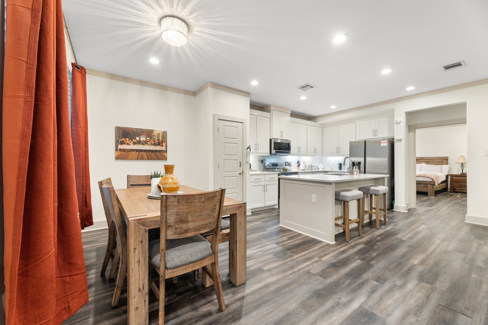 A modern kitchen with white cabinets, a central island with stools, and a dining area with a wooden table and chairs.