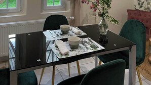 Un comedor con una mesa dispuesta para dos, un jarrón con flores y una ventana con cortinas.
