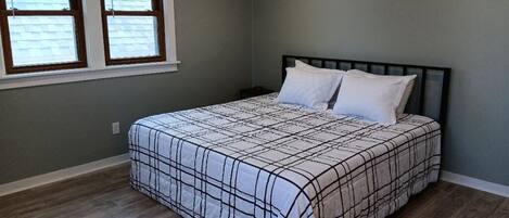 A bedroom with a bed, two windows, and a wooden floor.