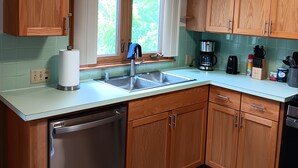 A modern kitchen with wooden cabinets, a stainless steel dishwasher, and a large window with curtains. - Beach House on the shores of Lake Michigan Near downtown Sheboygan (Sheboygan)