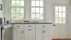 A kitchen with white cabinets, a countertop, and a window with a view of trees.