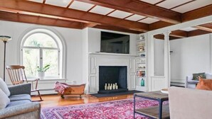 A spacious living room with a fireplace, wooden beams, and a large window.