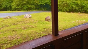 Blick von einer überdachten Terrasse mit Holzgeländer auf eine Straße und üppige, grüne Bäume.